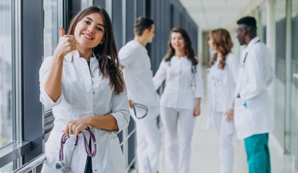 young-female-doctor-with-thumbs-up-gesture-standing-corridor-hospital-min young-female-doctor-with-thumbs-up-gesture-standing-corridor-hospital-min